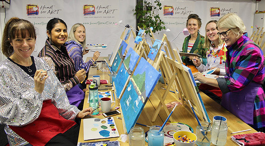 happy ladies in front of easels with brushes all art materials creating their island bay paintings