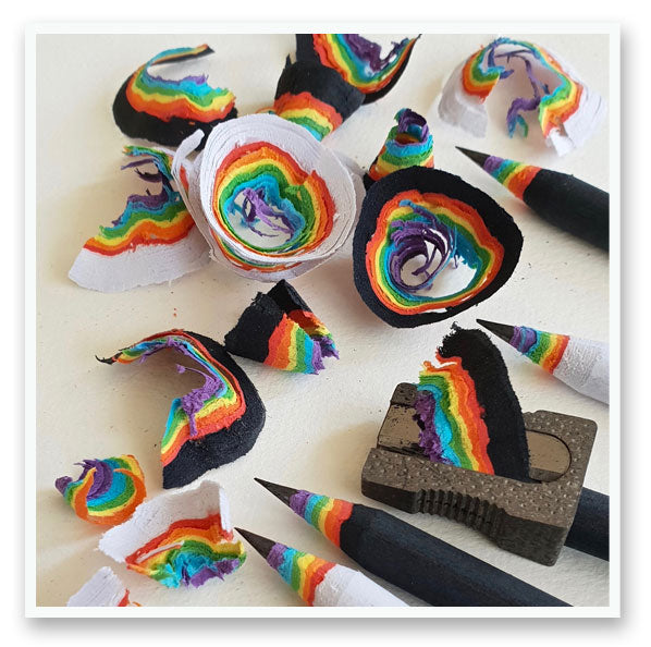 four rainbow pencils with pencil sharpener next to rainbow pencil shavings rainbow wood shavings